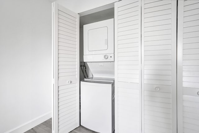 clothes washing area featuring laundry area, light wood-style flooring, stacked washer and clothes dryer, and baseboards