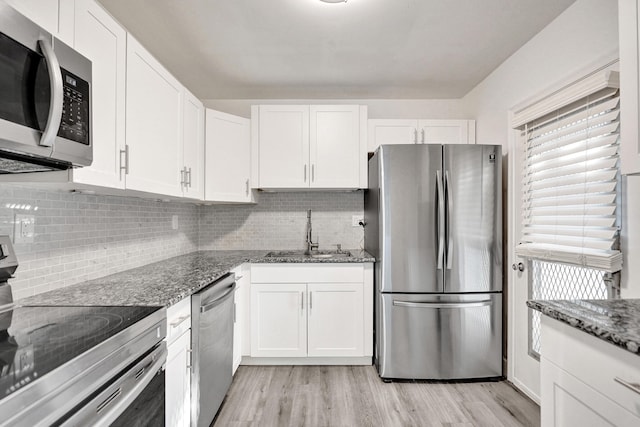 kitchen featuring white cabinets, dark stone counters, light wood-style flooring, appliances with stainless steel finishes, and a sink