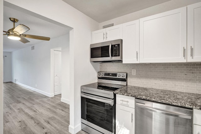 kitchen with dark stone countertops, appliances with stainless steel finishes, white cabinets, and backsplash