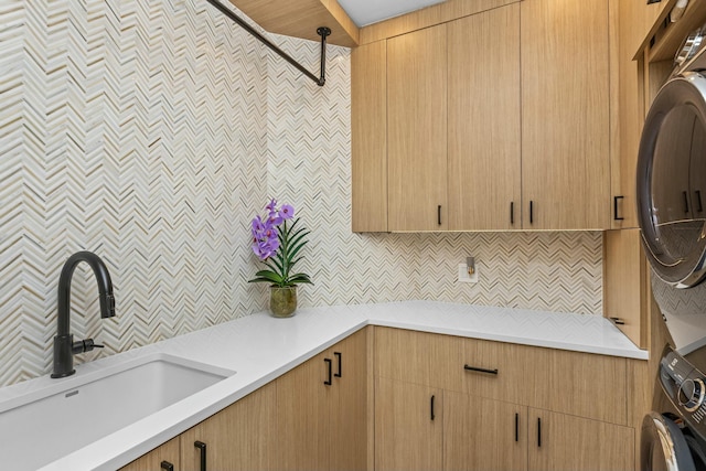 kitchen with stacked washing maching and dryer, decorative backsplash, light countertops, and a sink