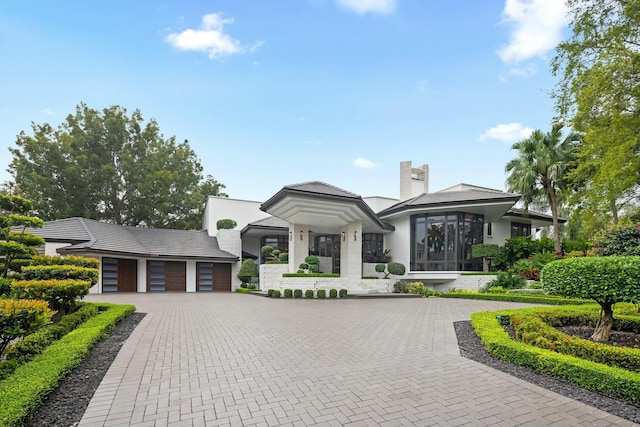 prairie-style home featuring a garage, decorative driveway, a chimney, and stucco siding