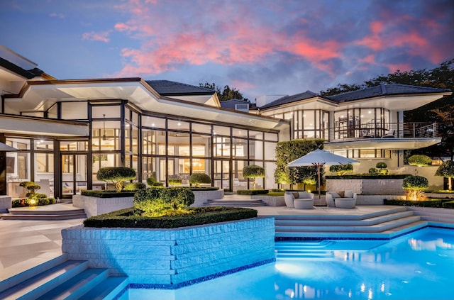 pool at dusk with an outdoor pool and a patio