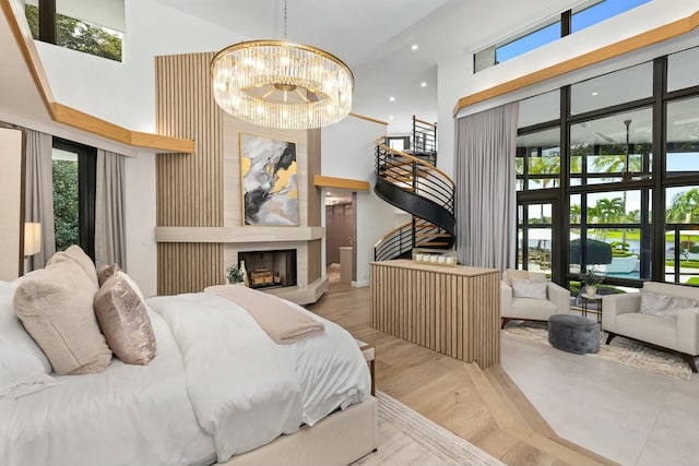 bedroom featuring a towering ceiling, an inviting chandelier, a fireplace, and wood finished floors