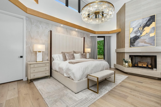 bedroom with wood finished floors, a large fireplace, a high ceiling, and an inviting chandelier