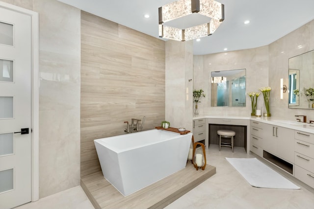 bathroom featuring a soaking tub, vanity, tile walls, and recessed lighting