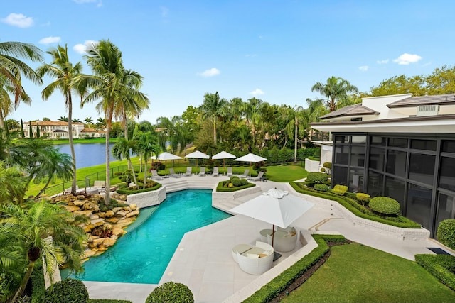 outdoor pool featuring a sunroom, a patio area, a lawn, and a water view