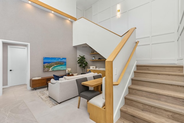 stairs with tile patterned flooring, a high ceiling, and a decorative wall