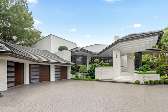 view of front facade featuring a tiled roof, decorative driveway, a garage, and a chimney