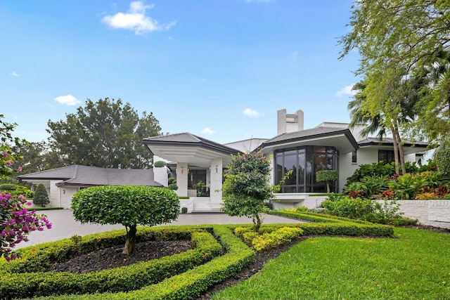 back of property featuring a yard, stucco siding, a sunroom, and a chimney