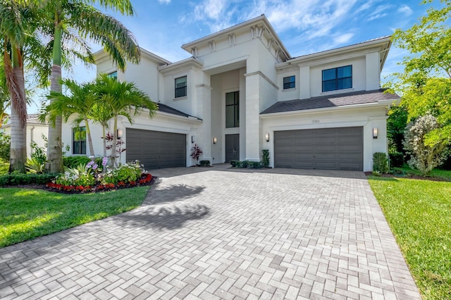 view of front facade featuring a front yard, decorative driveway, an attached garage, and stucco siding