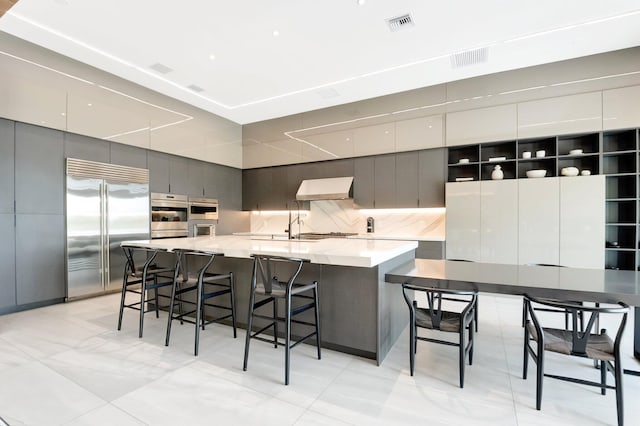 kitchen with tasteful backsplash, appliances with stainless steel finishes, modern cabinets, under cabinet range hood, and a kitchen bar