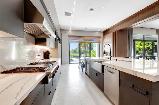 kitchen with decorative backsplash, light stone counters, appliances with stainless steel finishes, under cabinet range hood, and a sink