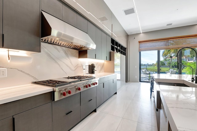 kitchen featuring visible vents, decorative backsplash, gray cabinetry, stainless steel gas cooktop, and exhaust hood