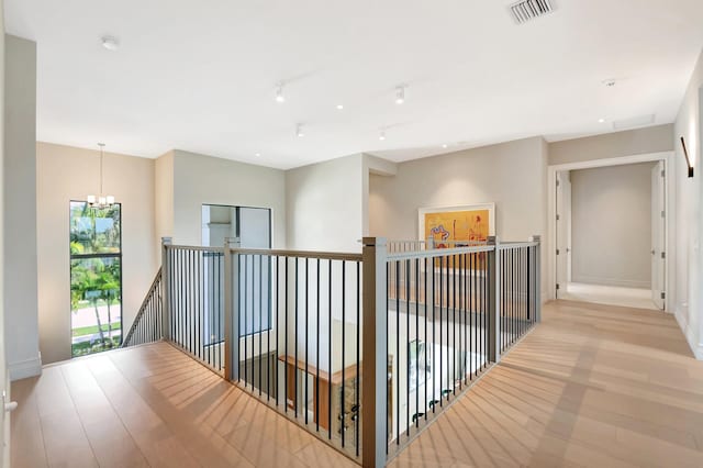 corridor with a notable chandelier, visible vents, an upstairs landing, wood finished floors, and baseboards