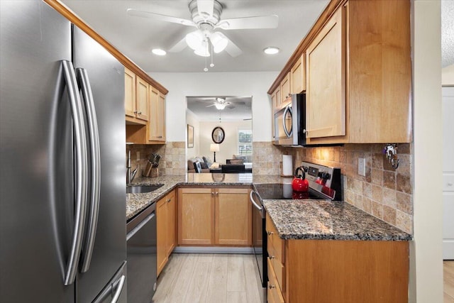 kitchen with dark stone counters, stainless steel appliances, a ceiling fan, light wood-type flooring, and backsplash