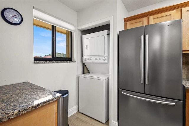 laundry room featuring baseboards, laundry area, light wood finished floors, and stacked washer / dryer