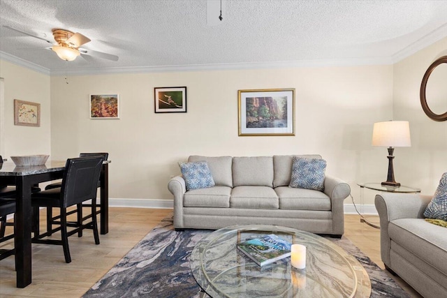 living area with crown molding, light wood-style flooring, a ceiling fan, a textured ceiling, and baseboards