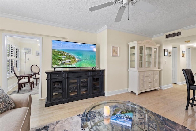 living room with light wood-style flooring, visible vents, a textured ceiling, and ornamental molding