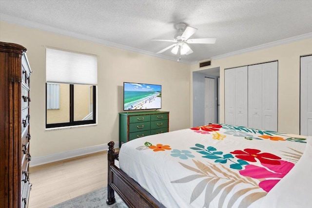 bedroom with visible vents, crown molding, a textured ceiling, light wood-type flooring, and multiple closets