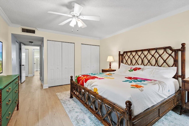 bedroom with visible vents, light wood-style flooring, ornamental molding, a textured ceiling, and two closets