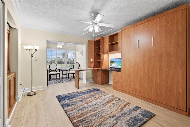 office area with a textured ceiling, built in desk, light wood-type flooring, and a ceiling fan