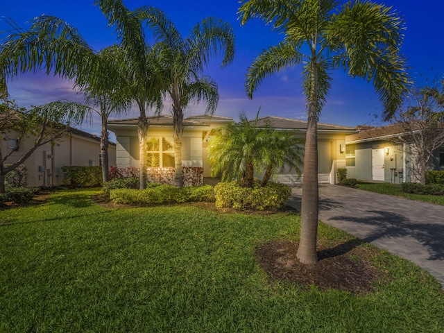 view of front of property featuring decorative driveway, an attached garage, a lawn, and stucco siding