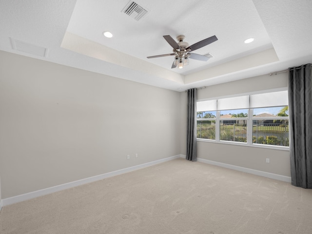 spare room featuring light carpet, a water view, visible vents, baseboards, and a tray ceiling