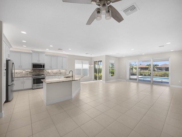 kitchen with visible vents, white cabinets, open floor plan, stainless steel appliances, and a sink