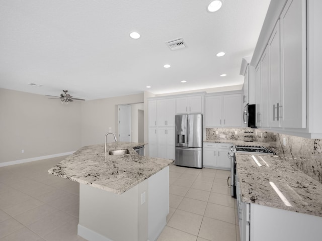 kitchen featuring light stone counters, a kitchen island with sink, a sink, white cabinetry, and appliances with stainless steel finishes