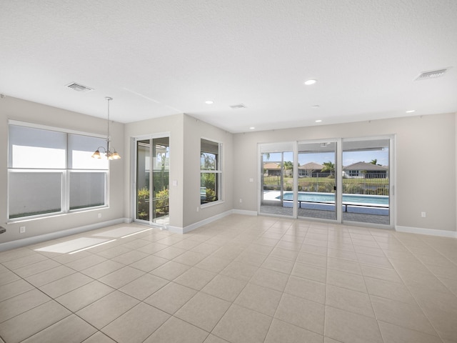 unfurnished room featuring a chandelier, light tile patterned flooring, visible vents, and baseboards