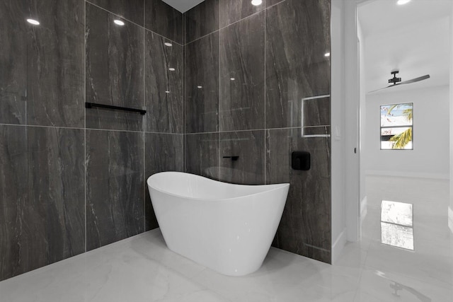 bathroom with a tub to relax in and tile walls