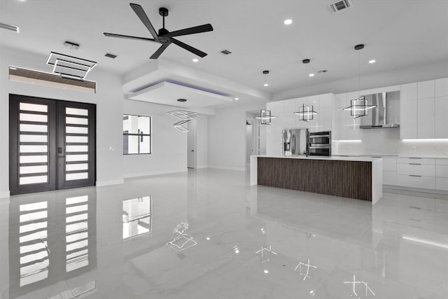 kitchen featuring appliances with stainless steel finishes, white cabinetry, wall chimney range hood, a spacious island, and french doors