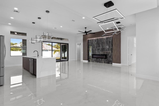 kitchen featuring appliances with stainless steel finishes, sink, light stone counters, decorative light fixtures, and a kitchen island with sink