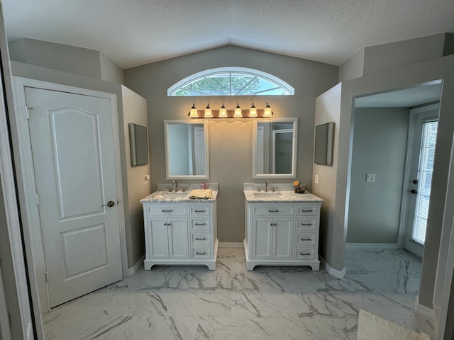 bathroom featuring baseboards, two vanities, marble finish floor, vaulted ceiling, and a sink