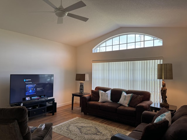 living area featuring ceiling fan, vaulted ceiling, a textured ceiling, wood finished floors, and baseboards