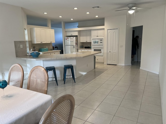 kitchen with light tile patterned floors, a peninsula, white appliances, tile counters, and decorative backsplash