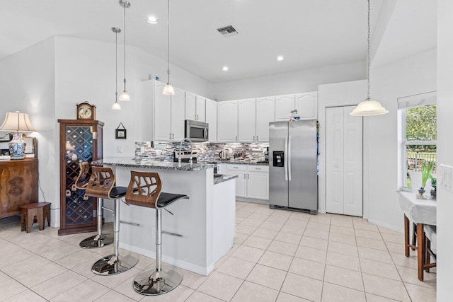 kitchen with light tile patterned floors, stainless steel appliances, a peninsula, backsplash, and dark stone countertops