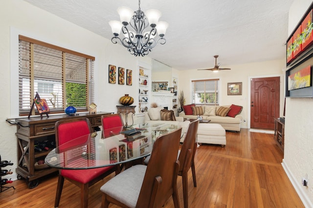 dining space featuring ceiling fan with notable chandelier, a fireplace, a textured ceiling, and wood finished floors