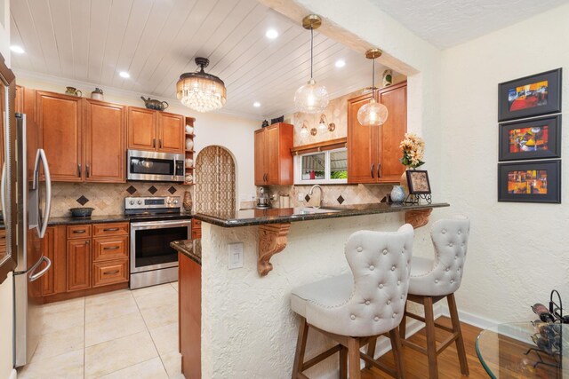 kitchen featuring a breakfast bar, brown cabinets, a peninsula, stainless steel appliances, and pendant lighting