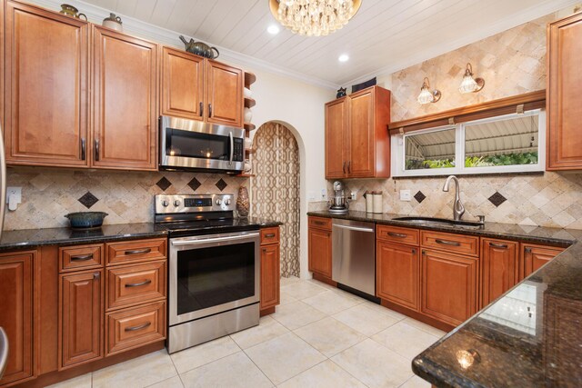 kitchen featuring a sink, ornamental molding, appliances with stainless steel finishes, dark stone counters, and brown cabinetry