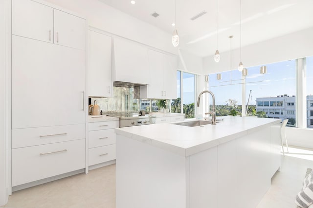 kitchen with a center island with sink, a sink, cooktop, light countertops, and white cabinets