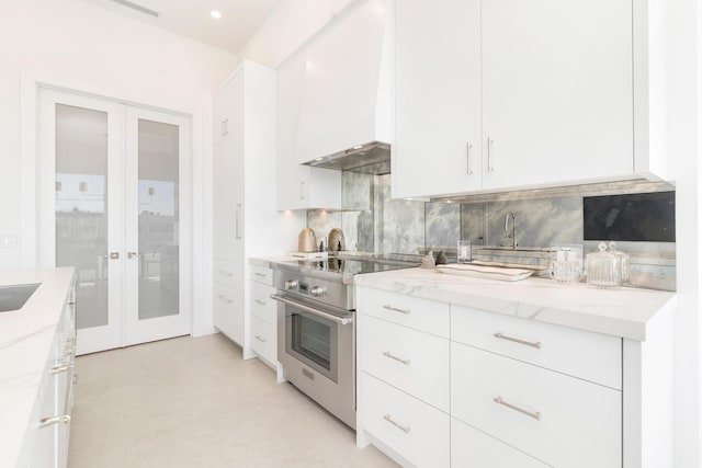 kitchen featuring stainless steel electric range oven, light stone counters, french doors, and premium range hood