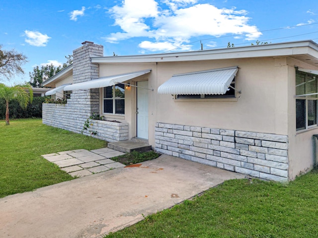 mid-century home with stone siding, a chimney, a front lawn, and stucco siding