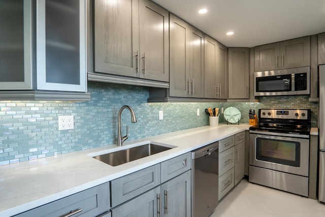 kitchen with light stone counters, a sink, stainless steel appliances, gray cabinetry, and backsplash