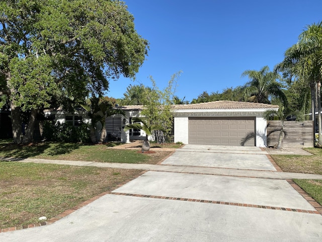 view of front of house featuring stucco siding, a front yard, a garage, driveway, and a tiled roof