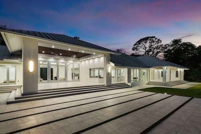 rear view of property featuring a standing seam roof, stucco siding, a patio, and metal roof