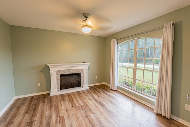 unfurnished living room with light wood-type flooring, a fireplace, a ceiling fan, and baseboards