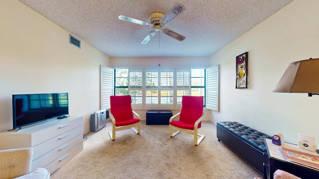 sitting room with ceiling fan, light carpet, and a textured ceiling