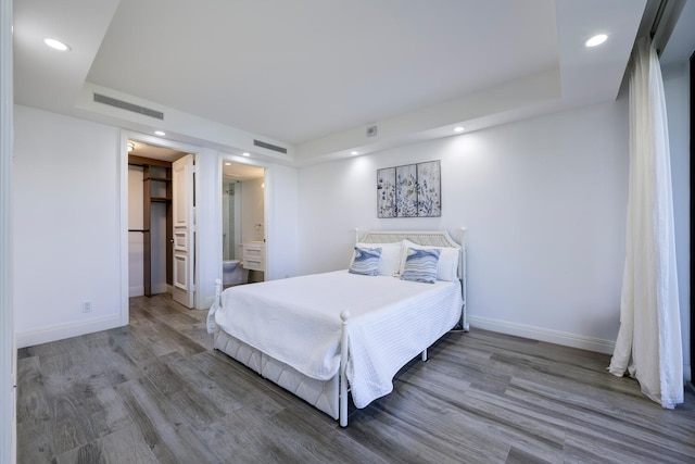 bedroom featuring recessed lighting, baseboards, wood finished floors, and a tray ceiling