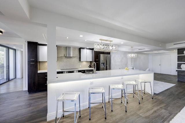 kitchen with stainless steel fridge, a sink, modern cabinets, wall chimney range hood, and light countertops